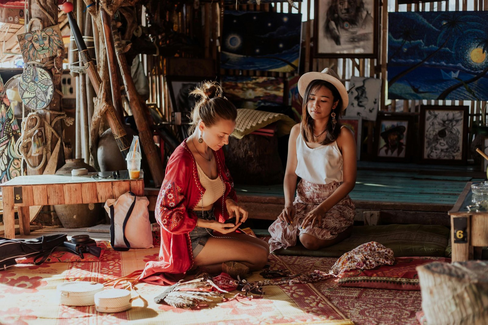 Two women crafting souvenirs in a vibrant Thai shop, surrounded by art and textiles.