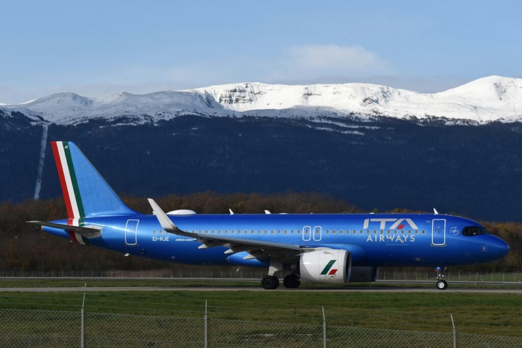 ITA Airways Airbus A320 taxiing at Geneva Airport with the Alps in the background.